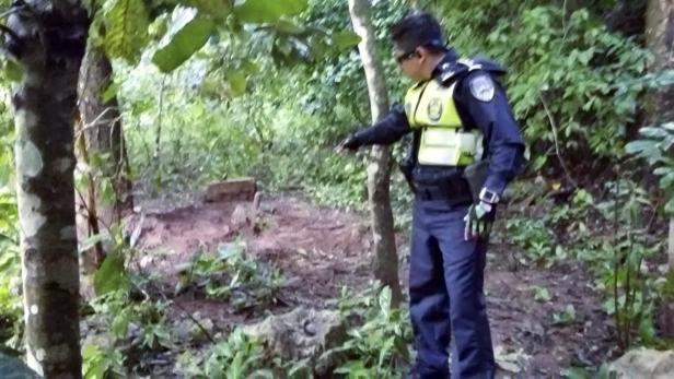 Ein Polizist in Uniform zeigt in einem Wald auf etwas im Unterholz.