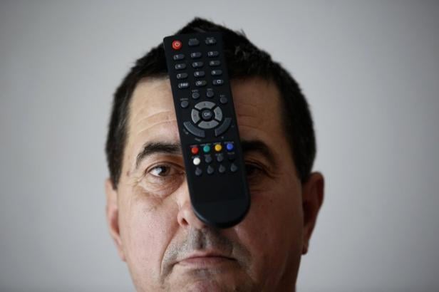 Ein Mann hält eine schwarze Fernbedienung vor sein Gesicht.