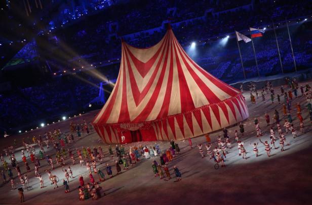Eine Zirkusvorstellung mit einem großen rot-weiß gestreiften Zelt und vielen Darstellern.