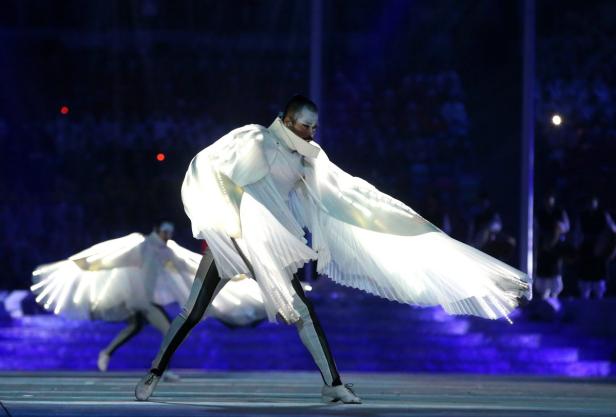 Ein Tänzer in einem weißen, flügelartigen Kostüm auf einer Bühne.