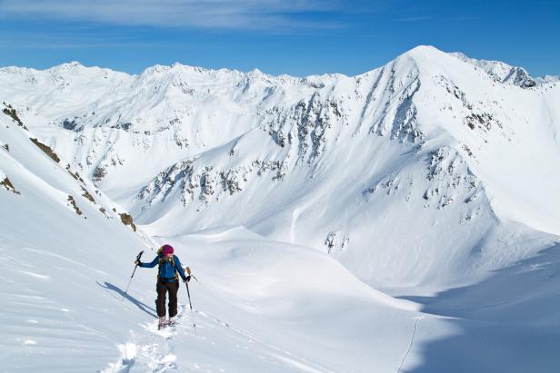 Eine Frau geht mit Skiern in einer verschneiten Berglandschaft.