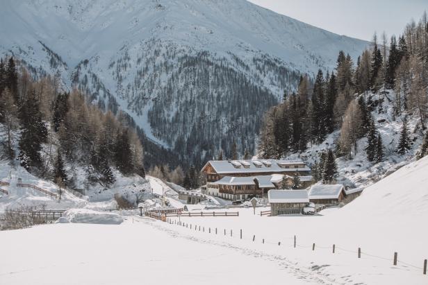 Ein verschneites Tal mit einem Hotel und bewaldeten Bergen im Hintergrund.