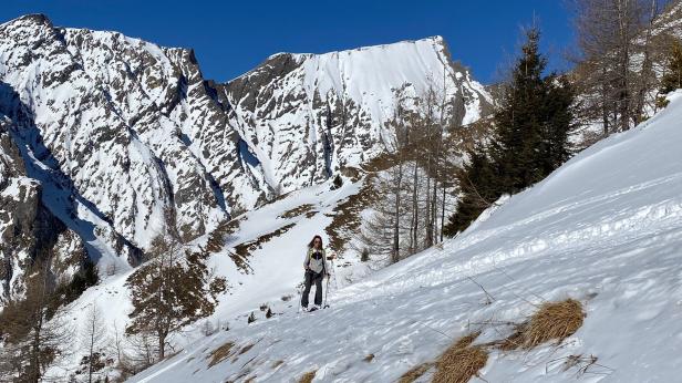 Eine Frau geht mit Schneeschuhen in einer verschneiten Berglandschaft.