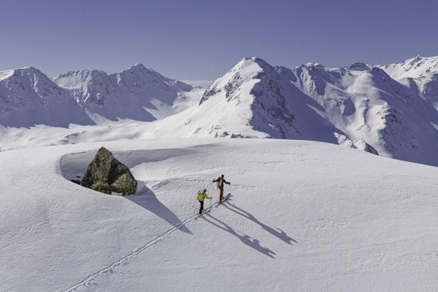 Zwei Skitourengeher steigen in einer verschneiten Berglandschaft auf.