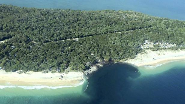 Luftaufnahme einer bewaldeten Insel mit Sandstrand und türkisfarbenem Wasser.