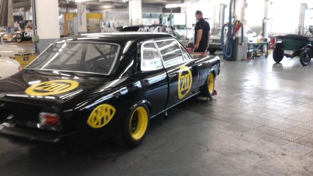 Ein schwarzer Opel mit gelben Akzenten steht in einer Werkstatt.