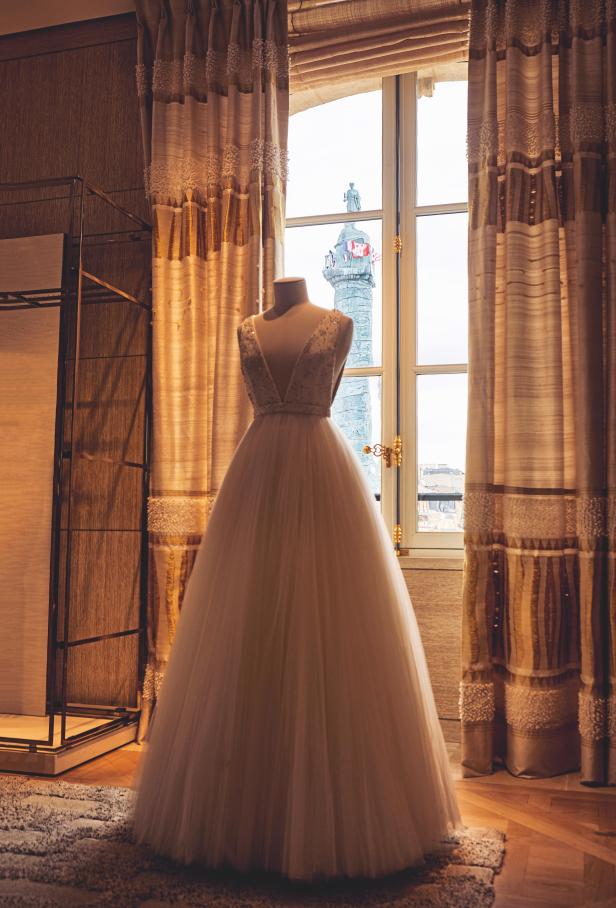 Ein weißes Brautkleid auf einer Schneiderpuppe vor einem Fenster mit Blick auf die Vendôme-Säule.