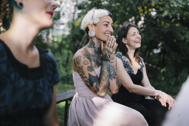Drei Frauen sitzen draußen und schauen lächelnd in die Ferne.