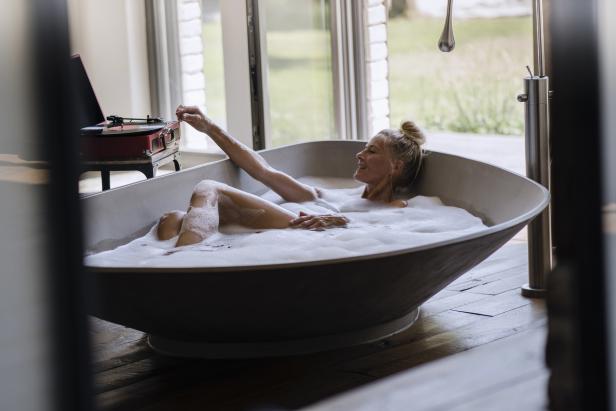 Eine Frau entspannt in einer mit Schaum gefüllten Badewanne und legt eine Schallplatte auf.