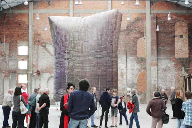 Besucher betrachten eine große, kissenförmige Installation in einer Backsteinhalle.