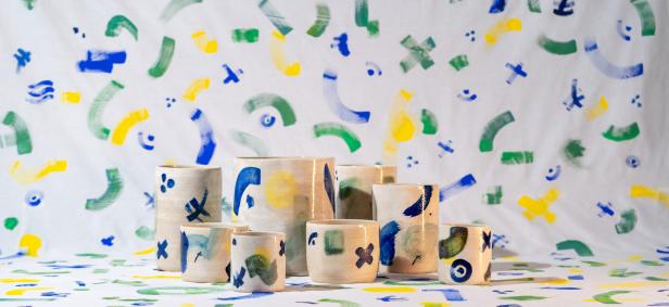 Eine Gruppe von bemalten Keramikbechern und -vasen auf einem farbenfrohen Hintergrund.