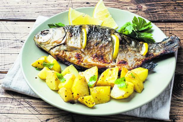 Baked fish carp with lemon greens and potatoes on a plate. Wooden background.