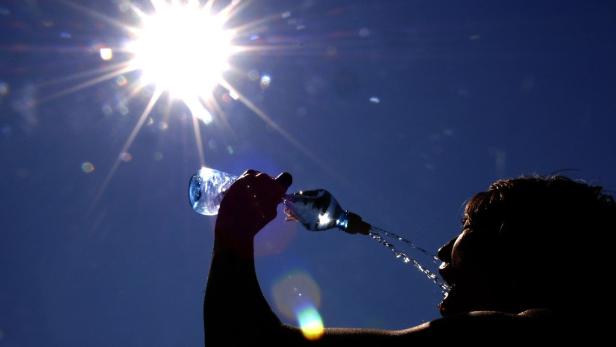 Eine Person trinkt an einem sonnigen Tag aus einer Wasserflasche.