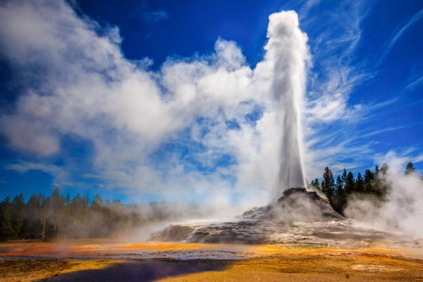 Ein Geysir bricht unter blauem Himmel und weißen Wolken aus.