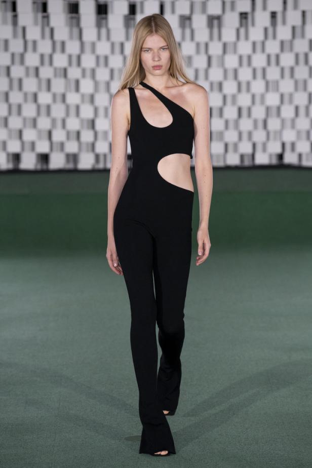 Ein Model präsentiert einen schwarzen, asymmetrischen Overall mit Cut-out auf dem Laufsteg.