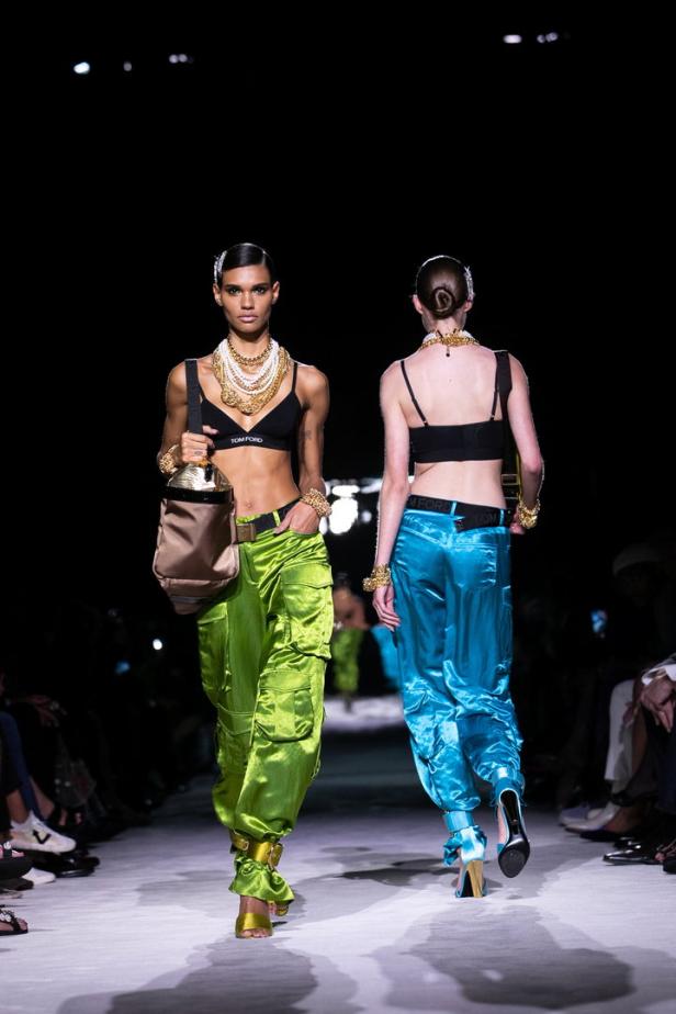 Zwei Models in glänzenden Hosen präsentieren Mode auf einem Laufsteg.