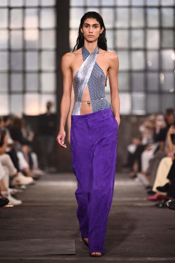 Eine Frau präsentiert ein blau-weiß gestreiftes Oberteil und eine violette Hose auf dem Laufsteg.