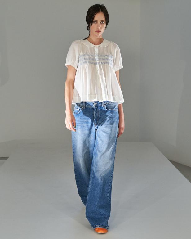 Eine Frau trägt eine weiße Bluse mit Jeans und orangefarbenen Schuhen.