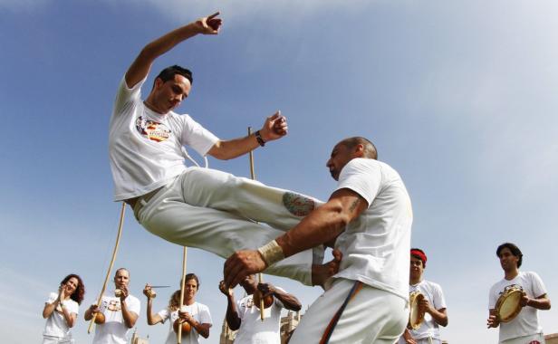 Zwei Männer führen Capoeira vor, während eine Gruppe von Musikern sie begleitet.