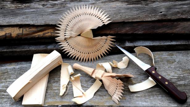 Ein Holzmesser und geschnitzte Holzspäne liegen auf einer Holzoberfläche.