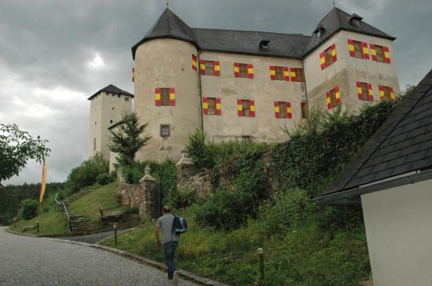 Ein Mann geht auf einer Straße in Richtung eines Schlosses mit rot-gelben Fensterläden.