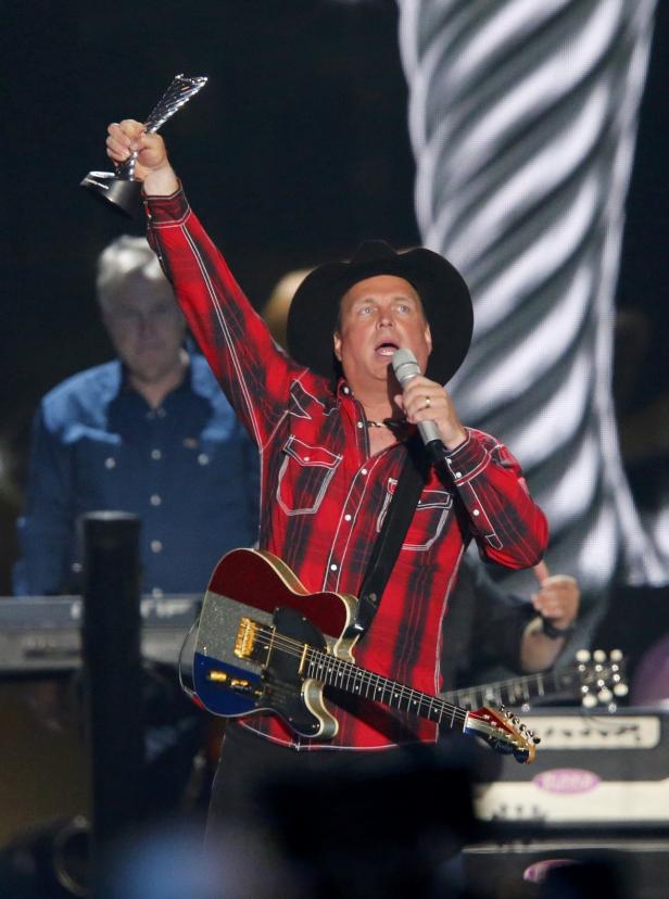 Garth Brooks hält eine Trophäe in der Hand und singt mit Gitarre auf der Bühne.
