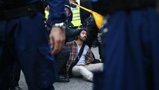 Ein Demonstrant sitzt auf dem Boden, umringt von Polizisten.