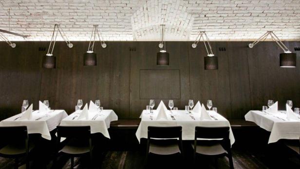 Gedeckte Tische in einem Restaurant mit dunkler Holzvertäfelung und weißen Backsteinwänden.