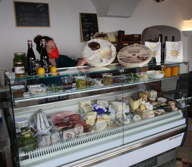 Eine Verkäuferin mit Maske präsentiert Käse und Feinkost in einer Vitrine.