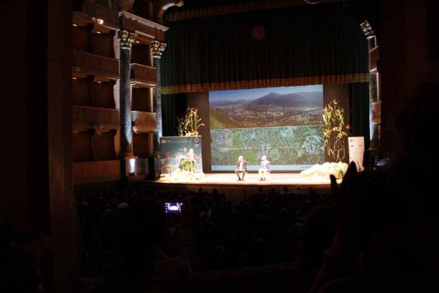 Zwei Personen sitzen auf einer Bühne vor einem großen Publikum.