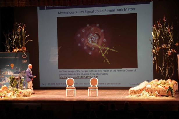 Ein Mann präsentiert eine Röntgenaufnahme des Perseus-Galaxienhaufens auf einer Bühne.