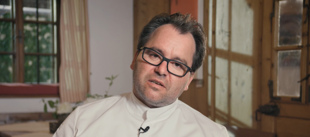 Ein Mann mit Brille und weißem Hemd vor einem Fenster.
