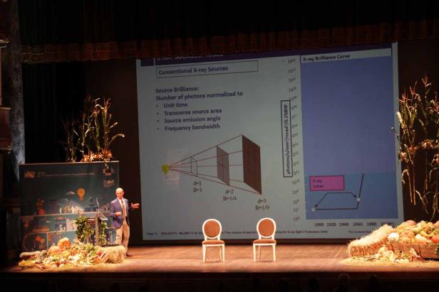 Ein Mann präsentiert eine Folie über Röntgenquellen auf einer Bühne mit herbstlicher Dekoration.