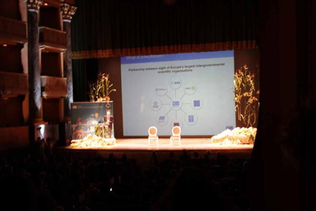 Ein Redner präsentiert auf einer Bühne eine Partnerschaft europäischer Organisationen.