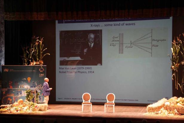 Ein Redner auf einer Bühne mit einer Präsentation über Max von Laue und Röntgenstrahlen.