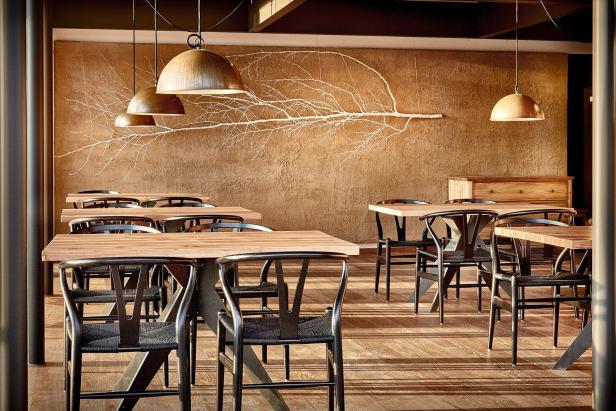 Ein Restaurant mit Holztischen, schwarzen Stühlen und einer Wanddekoration in Form eines Astes.
