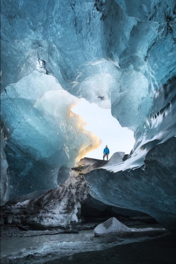 Ein Mann steht in einer Eishöhle mit blauem Eis und einem kleinen Bach.