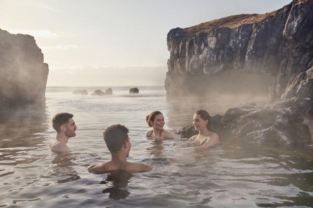 Eine Gruppe von Menschen entspannt sich in einem geothermalen Bad mit Felsen im Hintergrund.