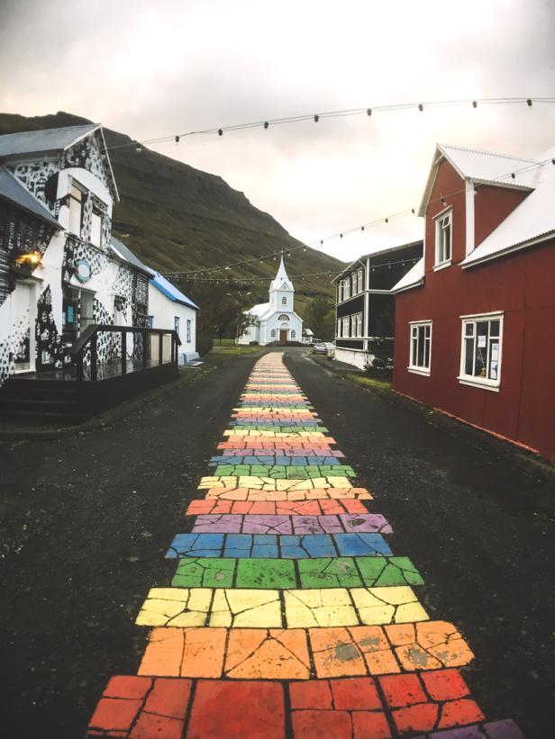 Eine Straße mit Regenbogenpflastersteinen führt zu einer Kirche in einem isländischen Dorf.