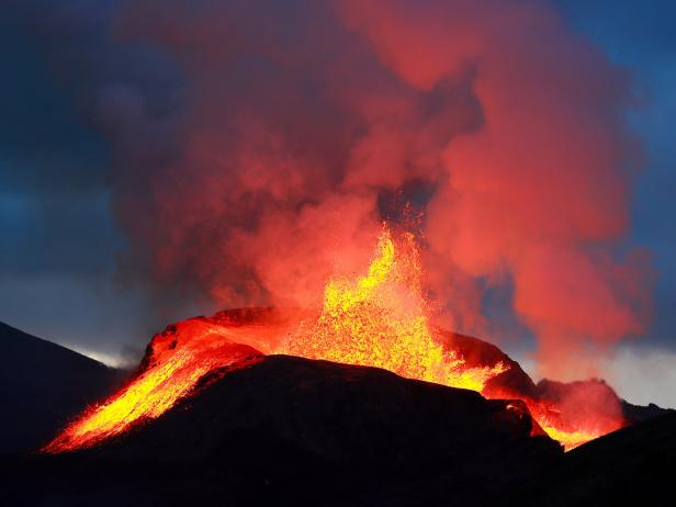 Ein Vulkan bricht aus und Lava fließt den Hang hinunter.