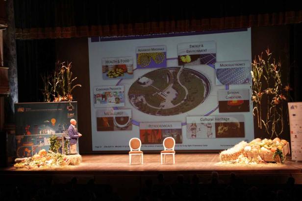 Ein Mann hält einen Vortrag auf einer Bühne, die mit Herbstdekorationen geschmückt ist.