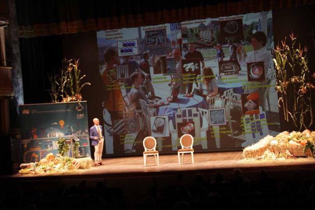 Ein Mann hält eine Präsentation auf einer Bühne mit herbstlicher Dekoration.
