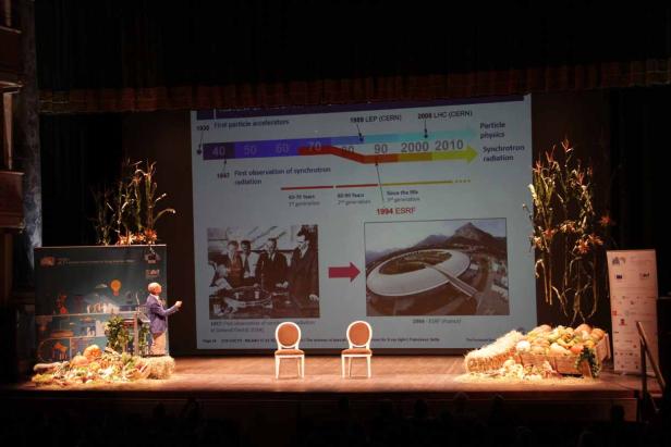 Ein Redner präsentiert eine Zeitleiste zur Teilchenphysik auf einer Bühne.
