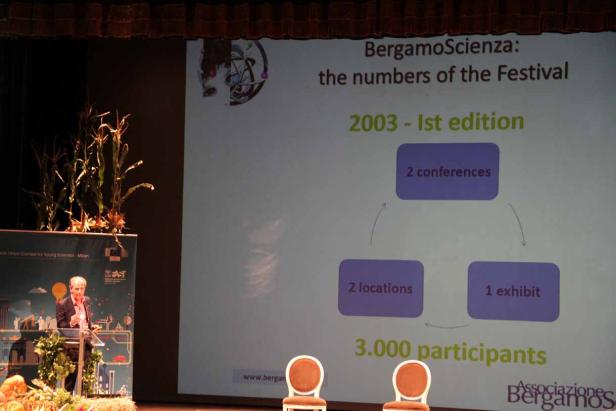 Ein Redner präsentiert die Zahlen des „BergamoScienza“-Festivals auf einer Bühne.