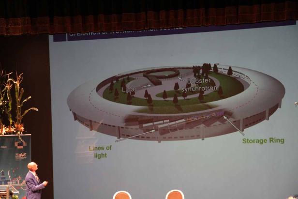 Ein Mann präsentiert eine Grafik eines Synchrotron-Speicherrings auf einer Leinwand.