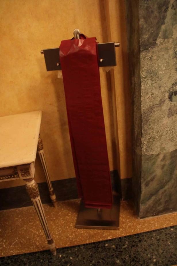 Eine rote Schärpe hängt an einem Ständer neben einem verzierten Tisch.