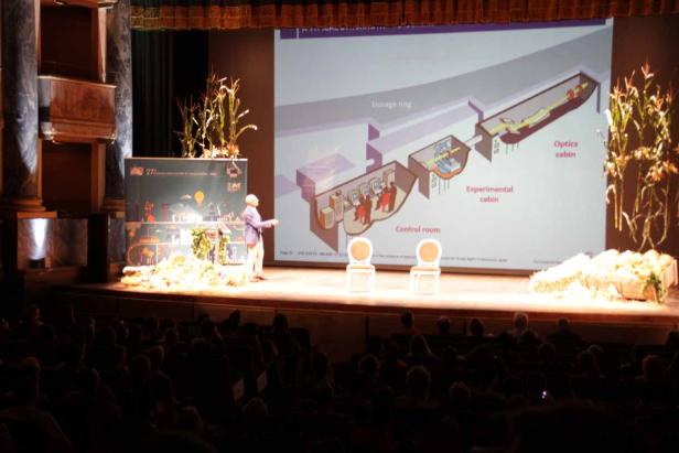 Ein Redner präsentiert ein Diagramm eines Teilchenbeschleunigers vor einem Publikum.