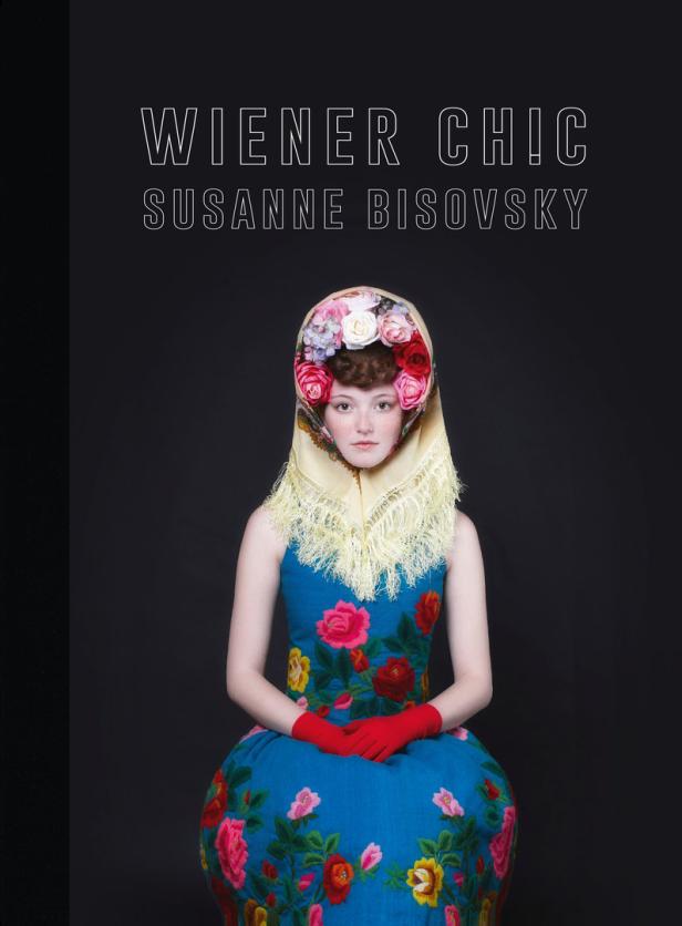 Eine Frau mit Blumenhaube und besticktem Kleid vor schwarzem Hintergrund.