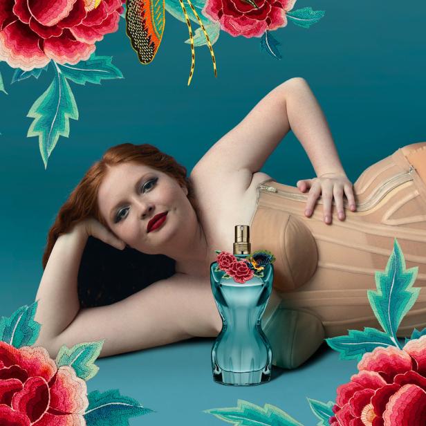 Eine Frau liegt neben einer Flasche des Parfüms Classique von Jean Paul Gaultier, umgeben von Blumen.