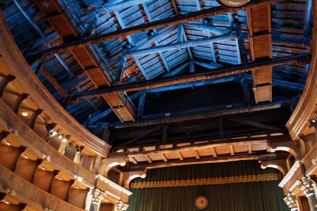 Blick in das Innere eines historischen Theaters mit Holzbalken und grünen Vorhängen.